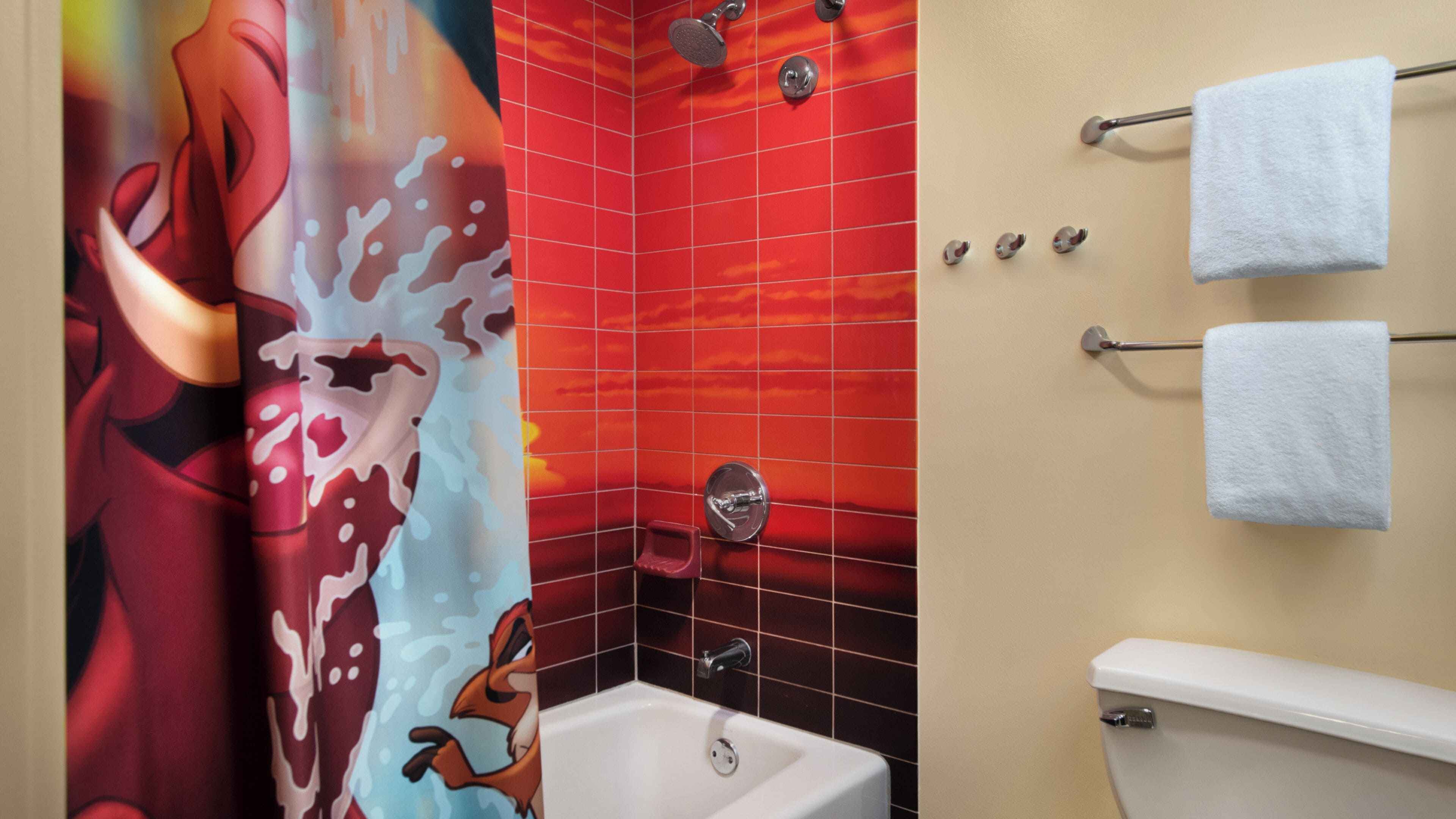 A bathroom with a red tiled shower wall, a white bathtub, and a towel rack with two towels.