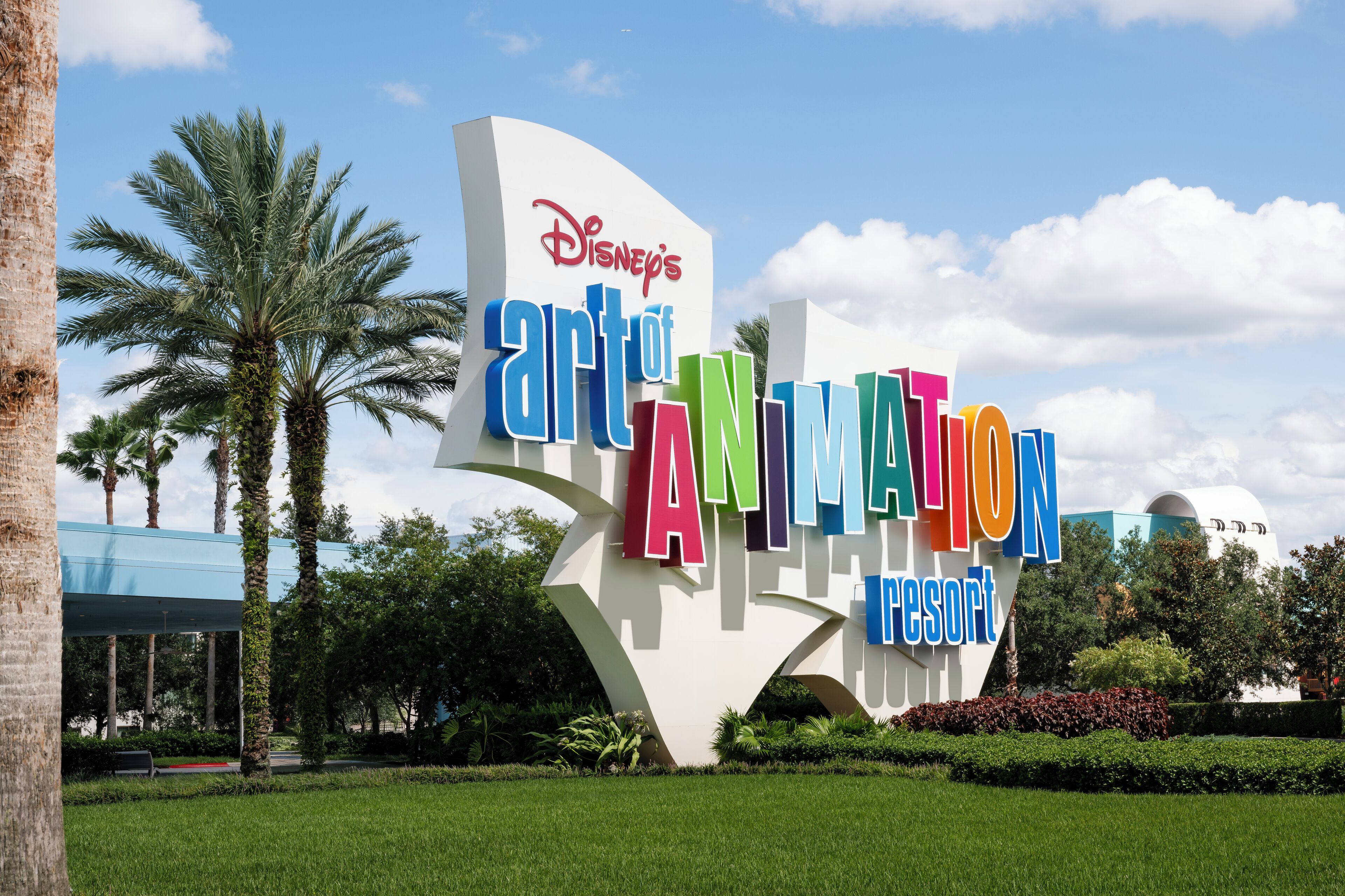 A large, colorful Disney Art of Animation Resort sign surrounded by palm trees and greenery.