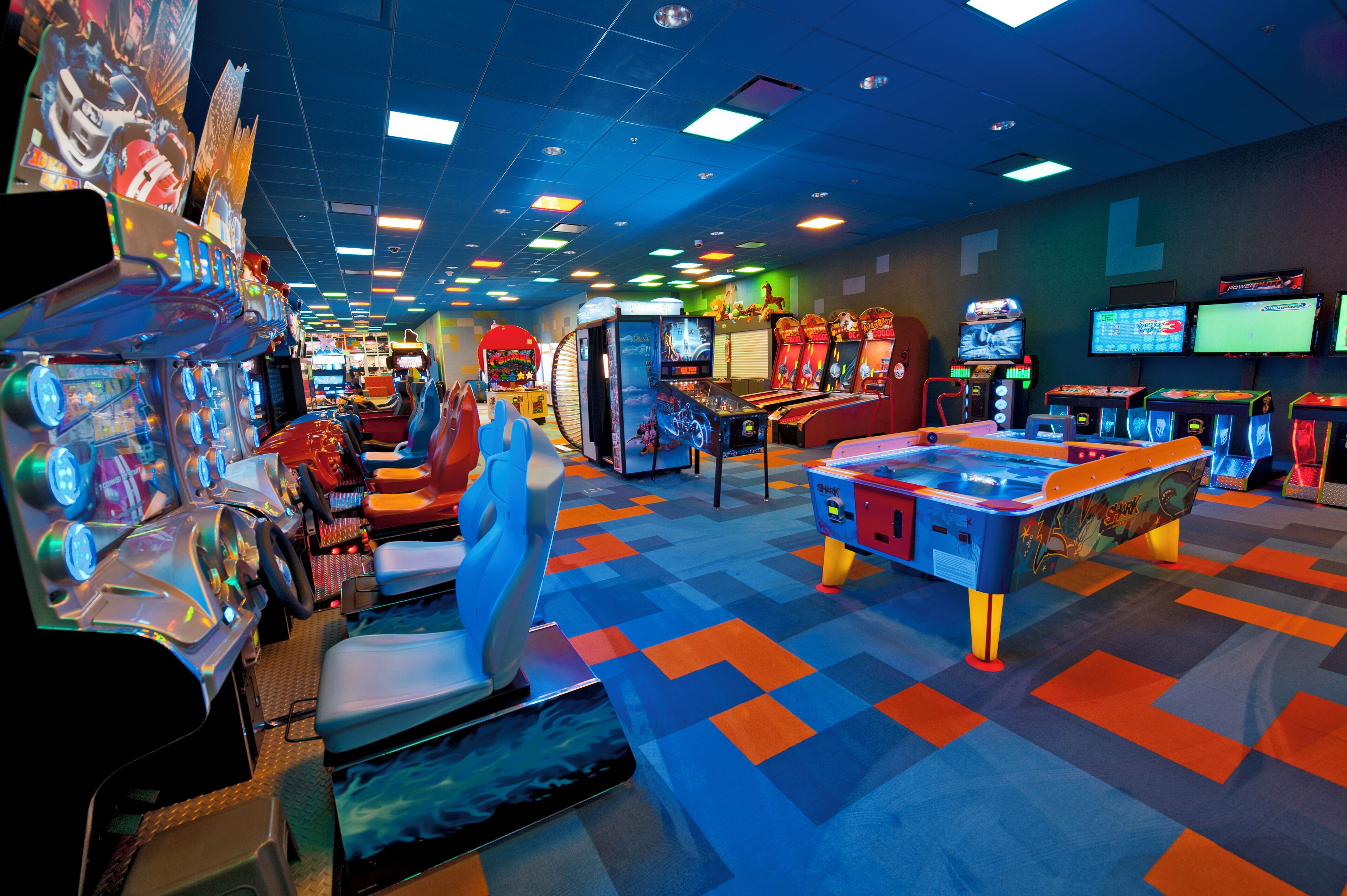 Une salle d’arcade avec différents jeux, une moquette colorée et de nombreux écrans fixés aux murs.
