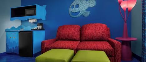 A room with a blue wall, a red sofa, green ottomans, a blue cabinet, and a pink lamp.