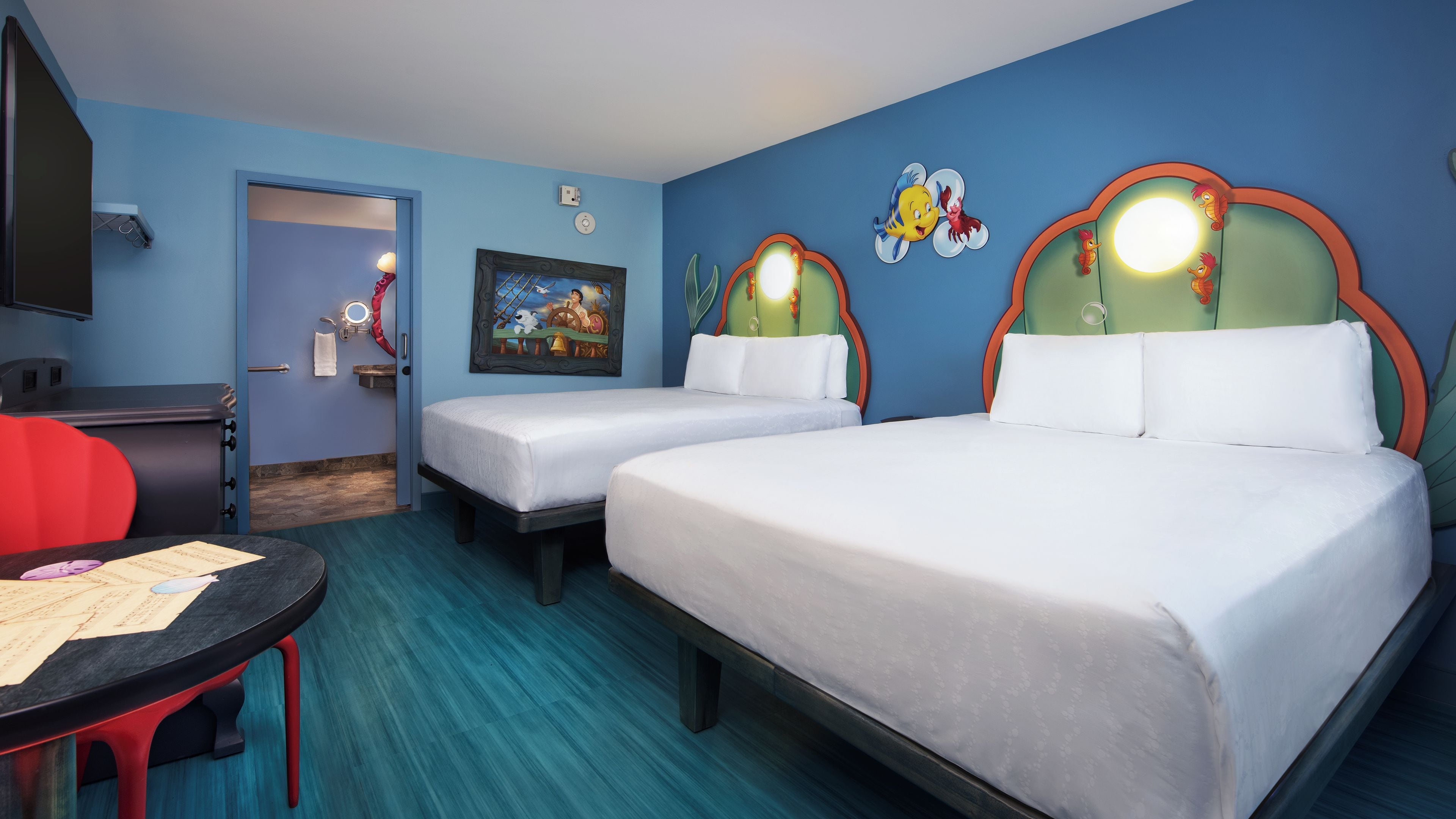 A hotel room with two beds, a desk, and a chair. There is a painting on the wall and a clock.