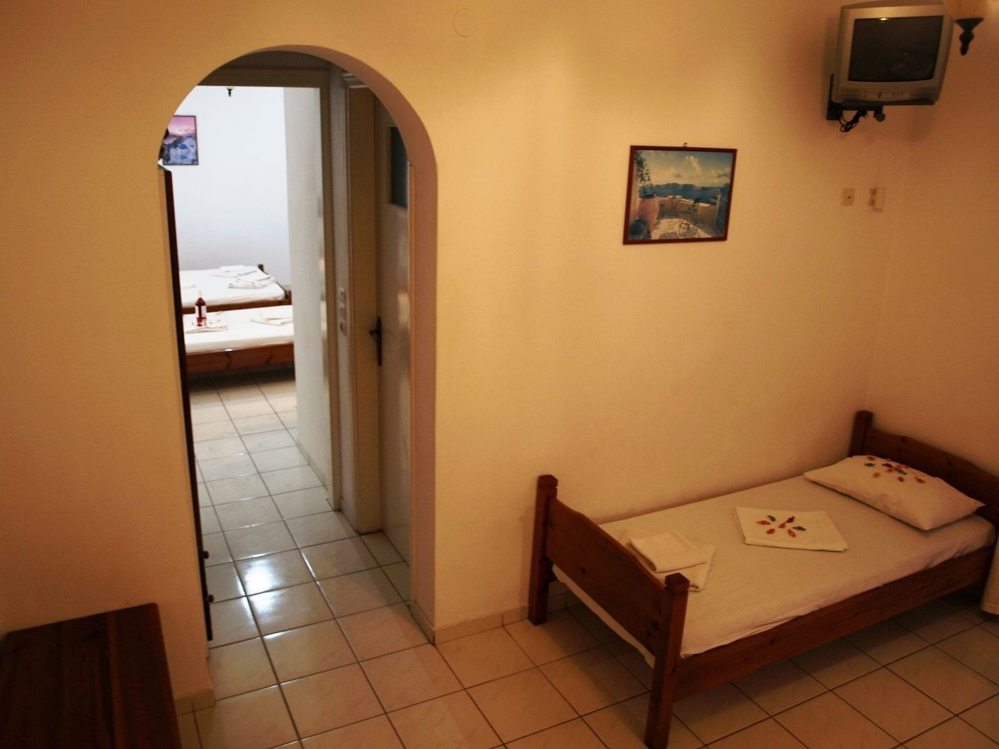 Habitació petita amb un llit individual, un llit de fusta, una televisió penjada a la paret i un quadre sobre el llit.