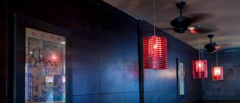 A dimly lit room with red seating, a framed poster on the wall, and hanging red lanterns.