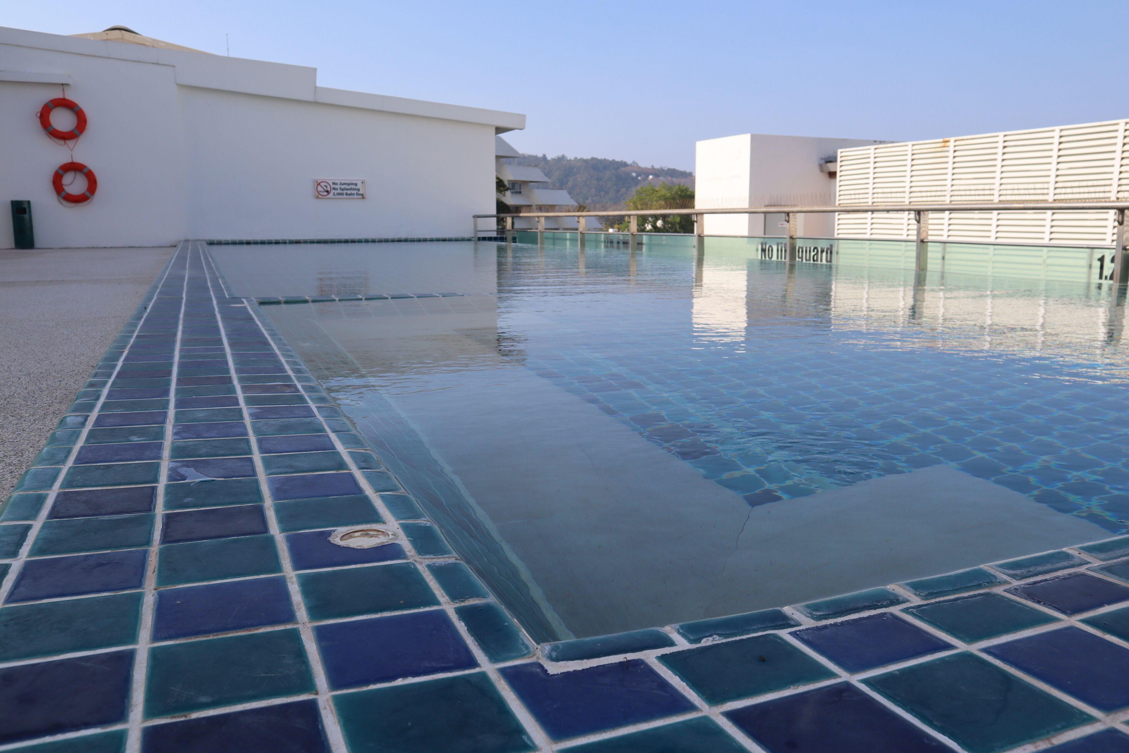 A swimming pool with a tiled edge, a lifebuoy, and a sign indicating no swimming.
