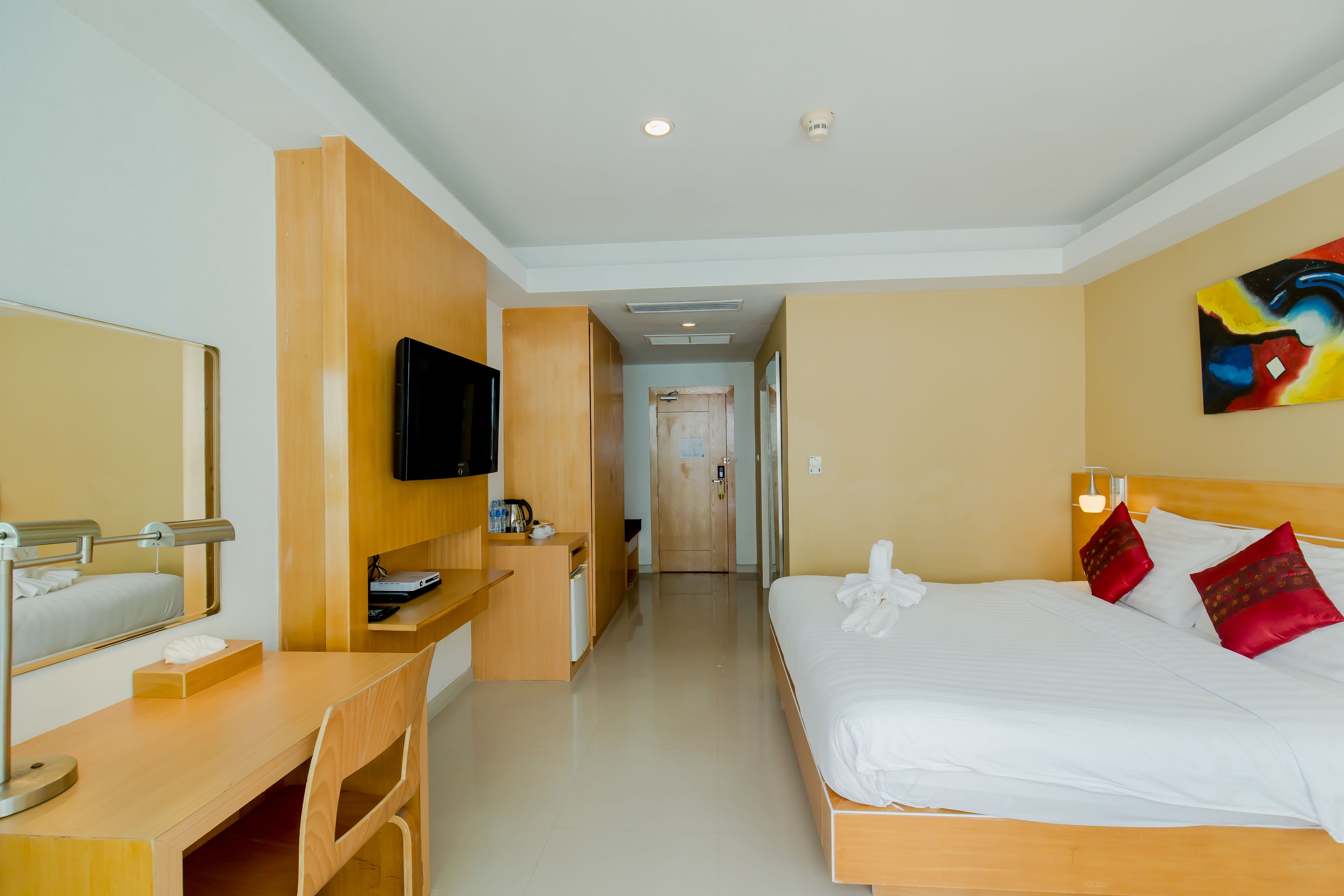 A hotel room with a bed, desk, chair, television, and a door leading to another room.