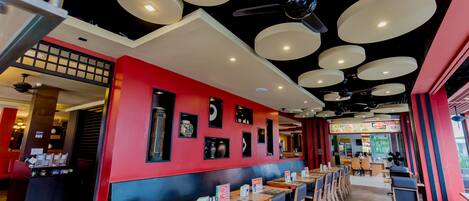 A restaurant with red walls, multiple ceiling lights, and a variety of seating arrangements including booths and tables.