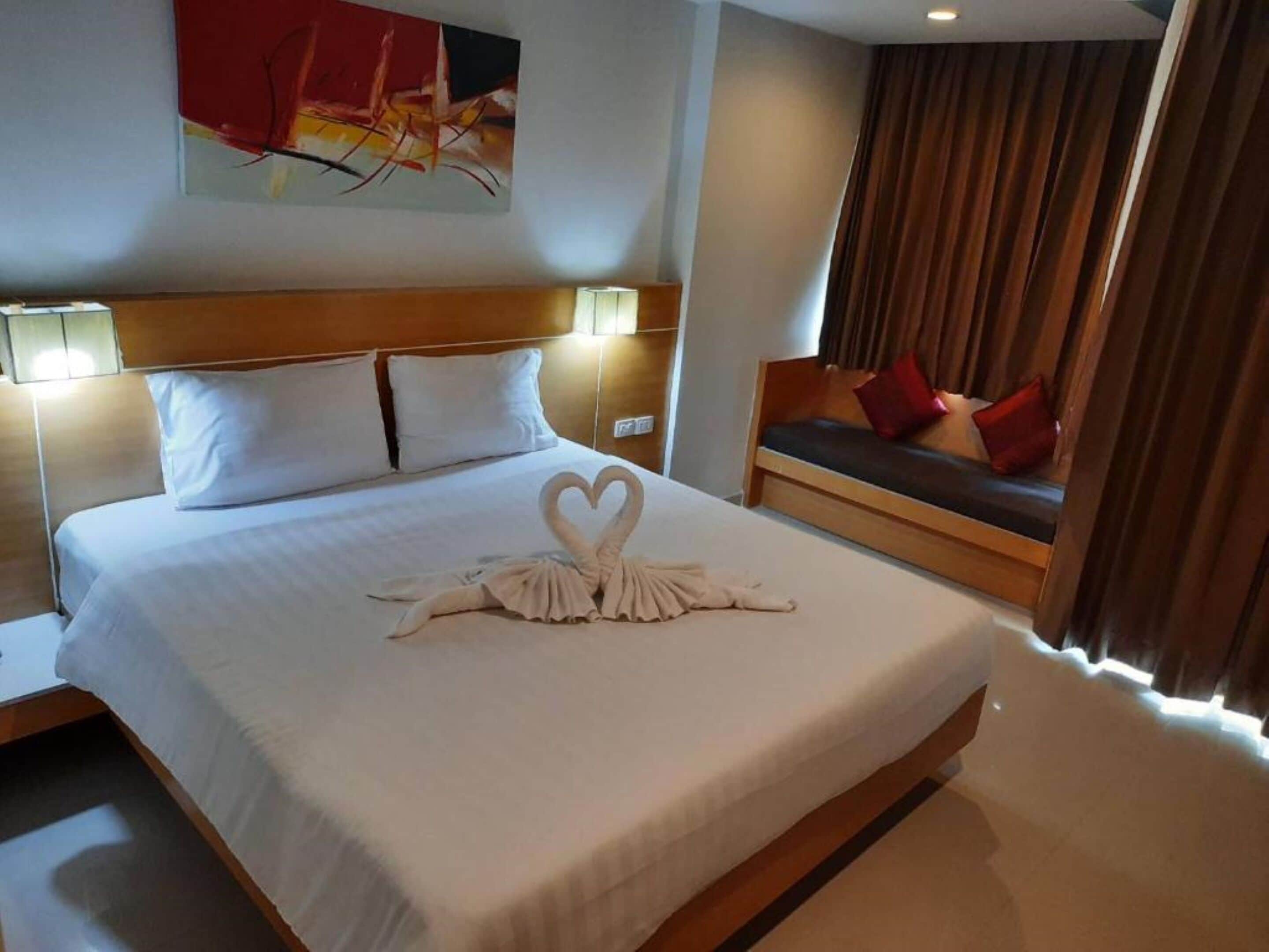 Ein Hotelzimmer mit einem ordentlich bezogenen Bett, einer Couch mit Kissen, einem Gemälde an der Wand und einem Fenster mit Vorhängen.