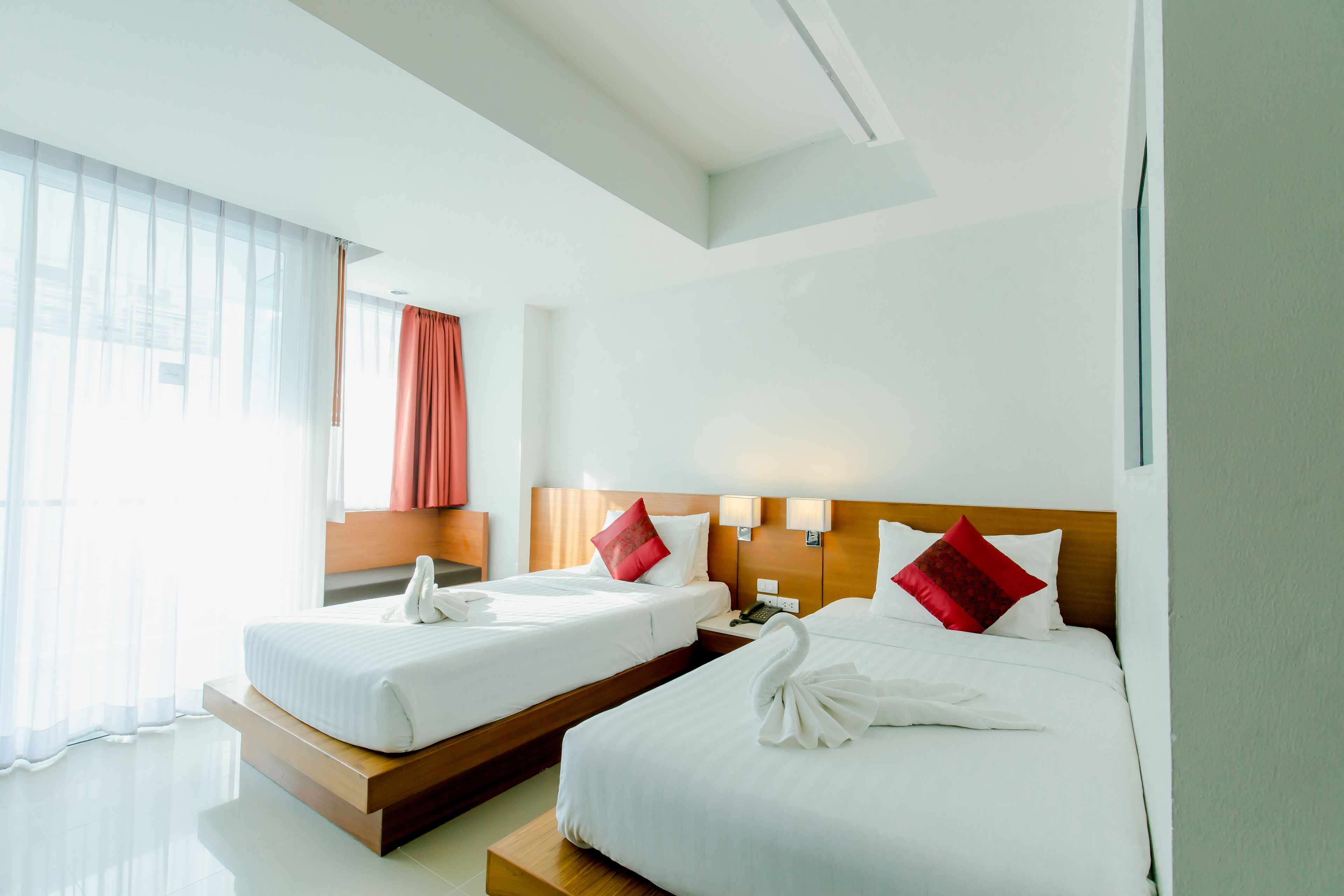 A hotel room with two beds, a wooden headboard, a telephone, and a window with sheer curtains.
