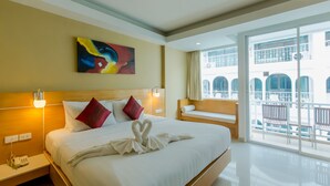 A hotel room with a large bed, a colorful abstract painting, a balcony with outdoor seating, and a view of the building's architecture. - Aspery Hotel (Patong)