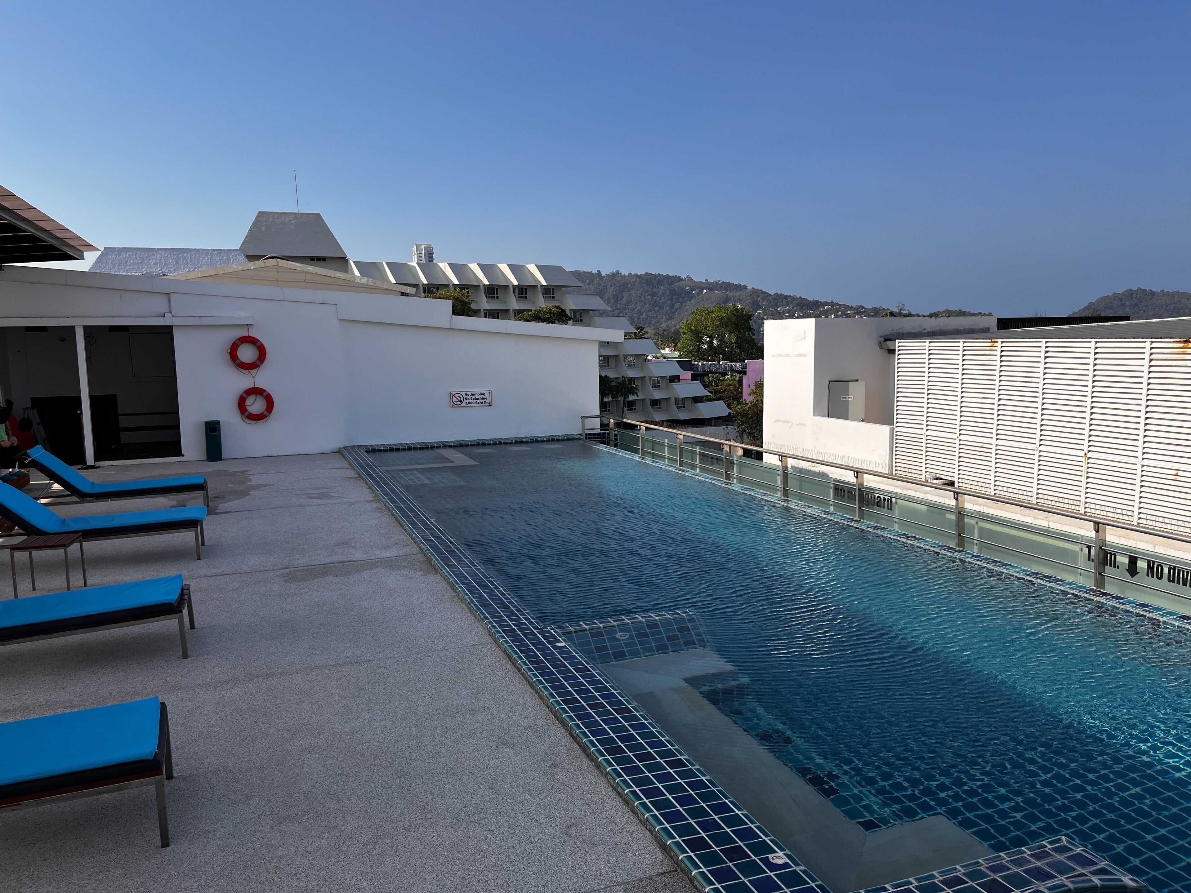 A rooftop pool with blue lounge chairs and a no-jumping sign.