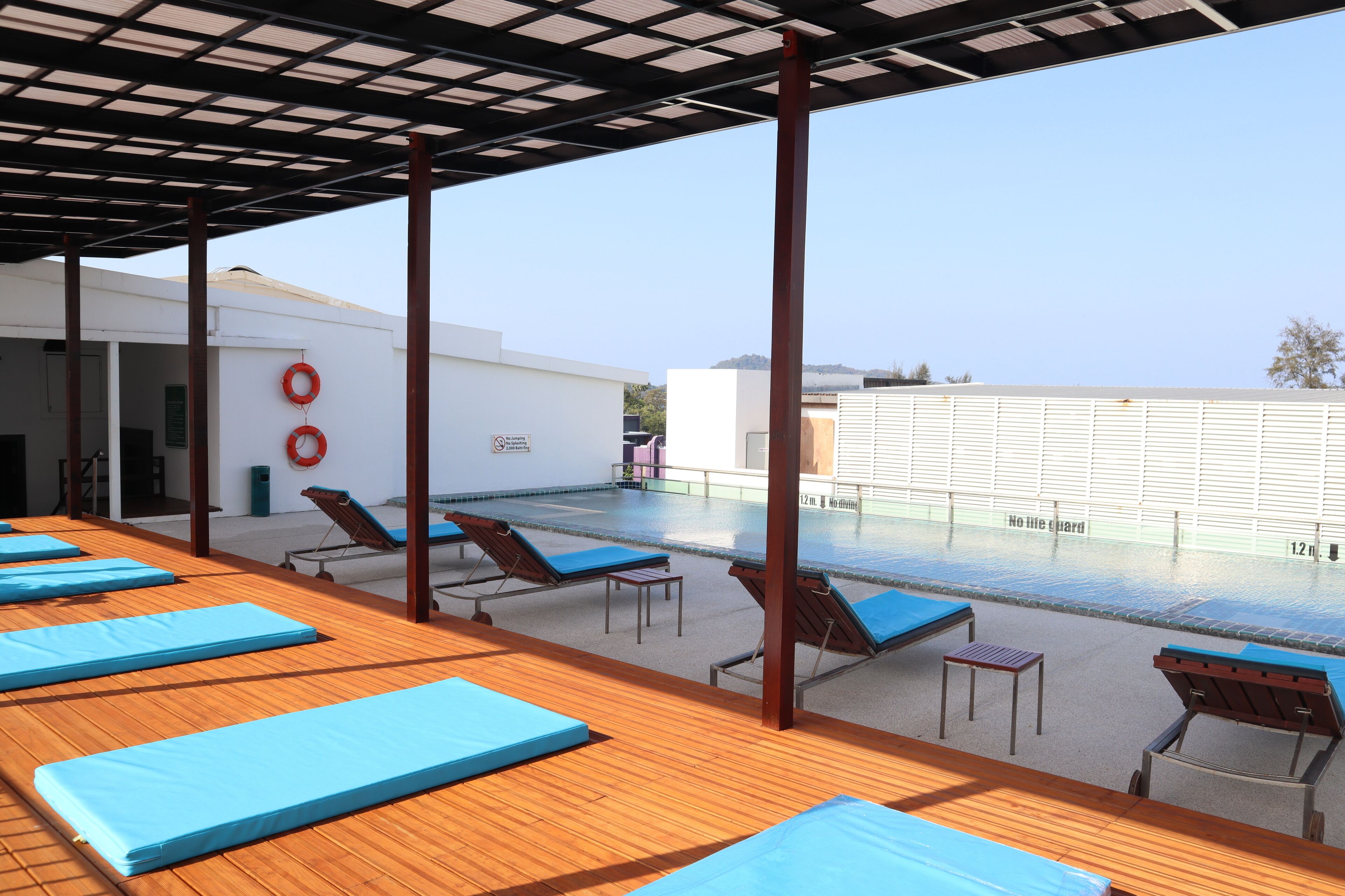 A rooftop pool area with sun loungers and blue mats, a lifebuoy, and a clear view of the city skyline.
