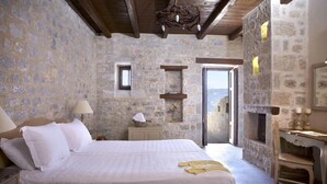 A bedroom with stone walls, a bed with white linens, a small bedside table, a chair, and a fireplace.