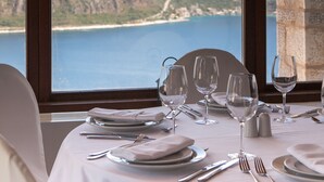 A table set for dining with a view of a coastal landscape through a stone arch window.