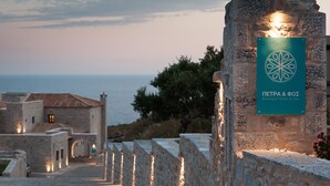 A stone pathway leading to a building with a sign for "PENTRA & ΦΣ Boutique Hotel & Spa" against a backdrop of the sea and a twilight sky.