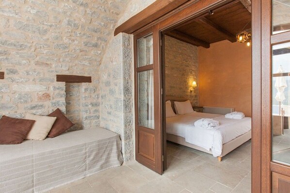 A bedroom with a stone wall, a wooden door, a bed with white linens, and a bench with cushions.