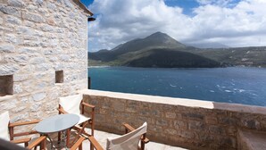 A stone building with a balcony overlooking a body of water and a mountain.