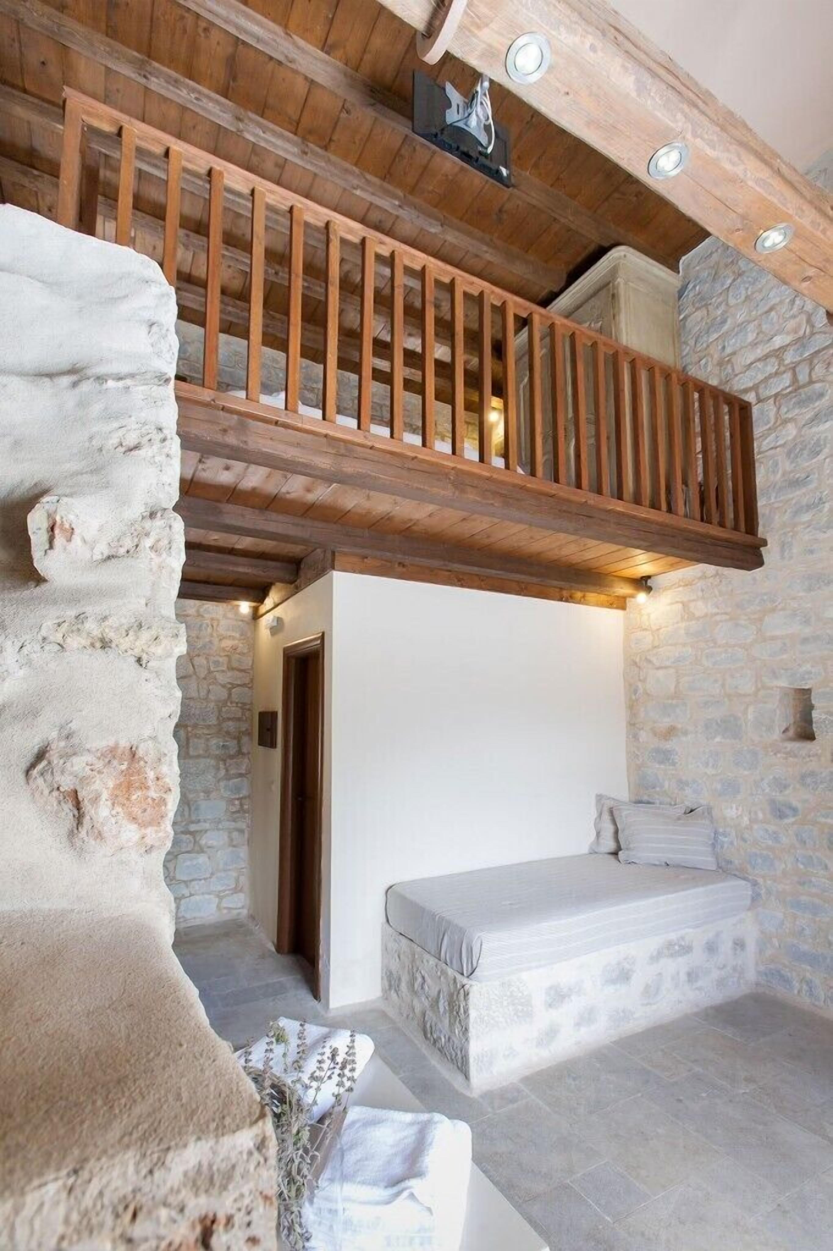 Un interior rústico con pared de piedra, balcón de madera y cama.