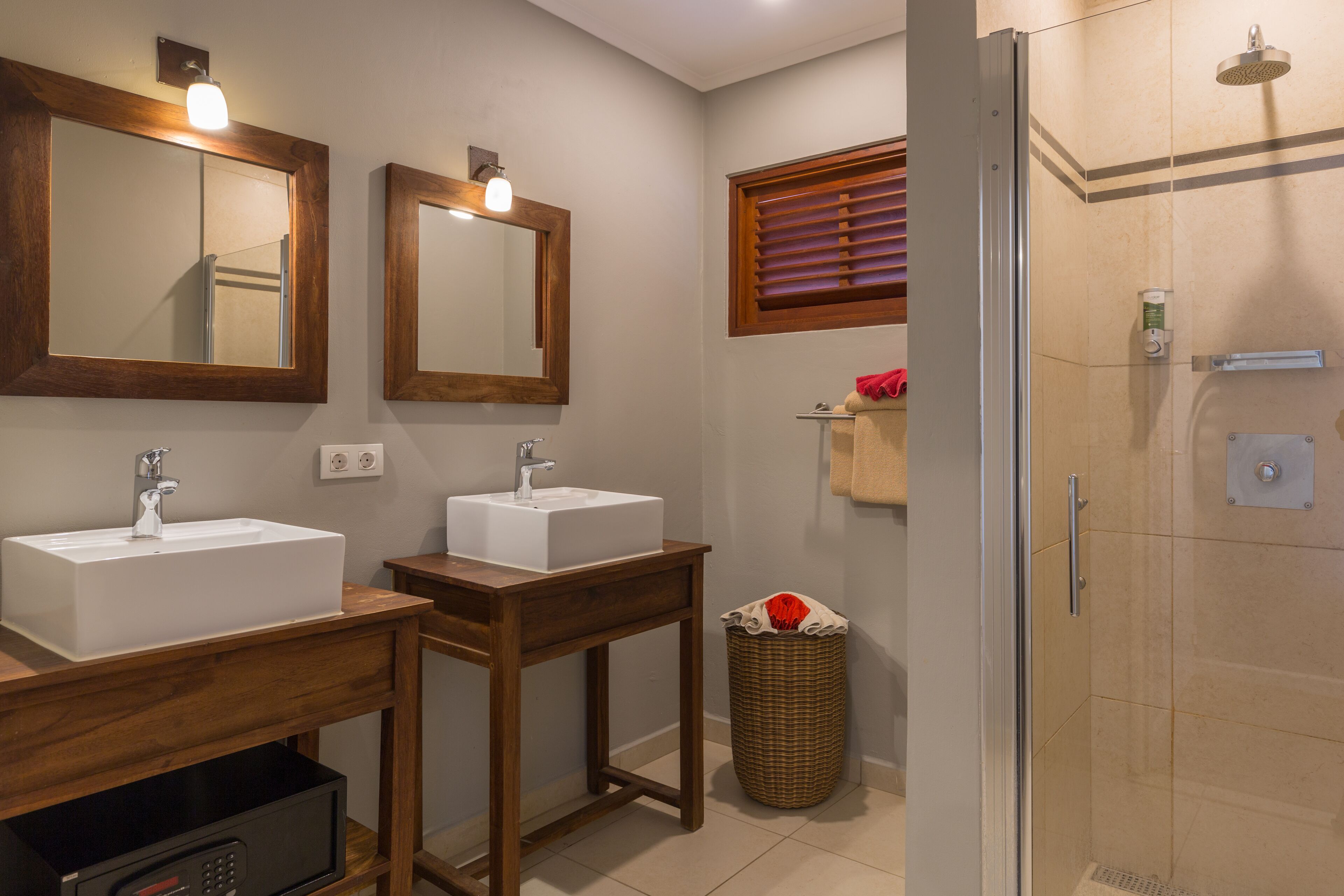 Un baño con dos lavamanos, un espejo, una ducha y un cubo de basura.