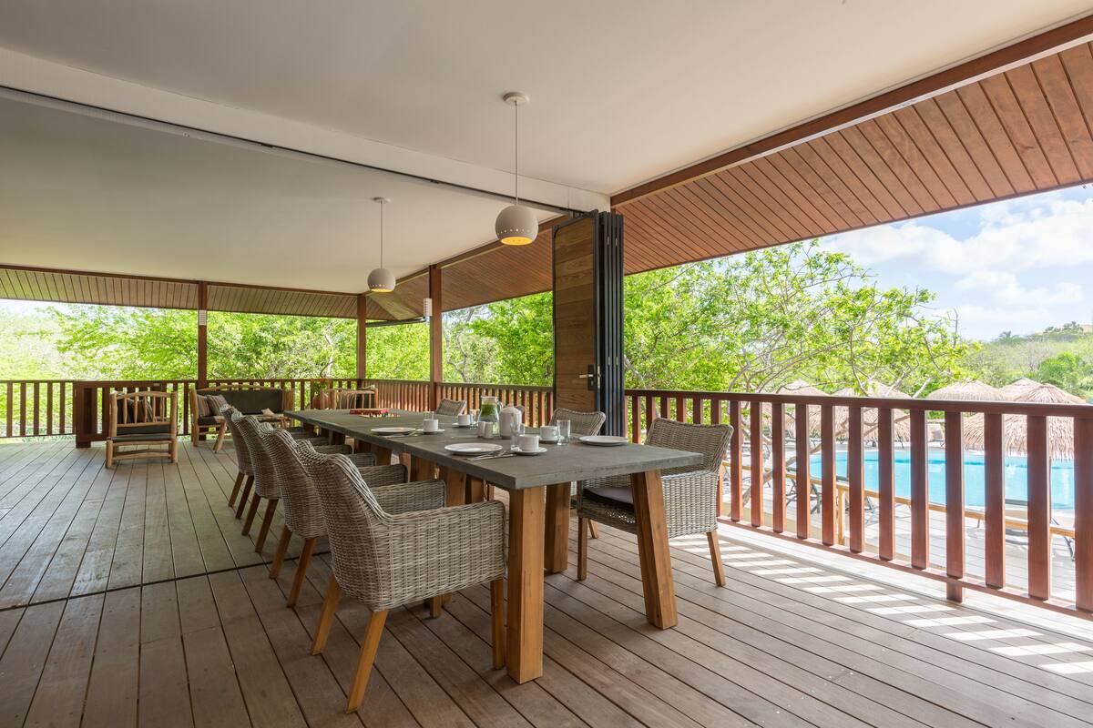A covered outdoor dining area with a pool in the background.