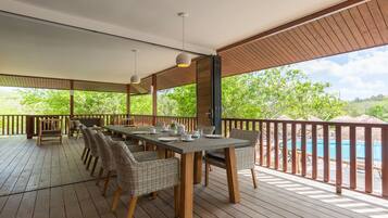 A covered outdoor dining area with a pool in the background.