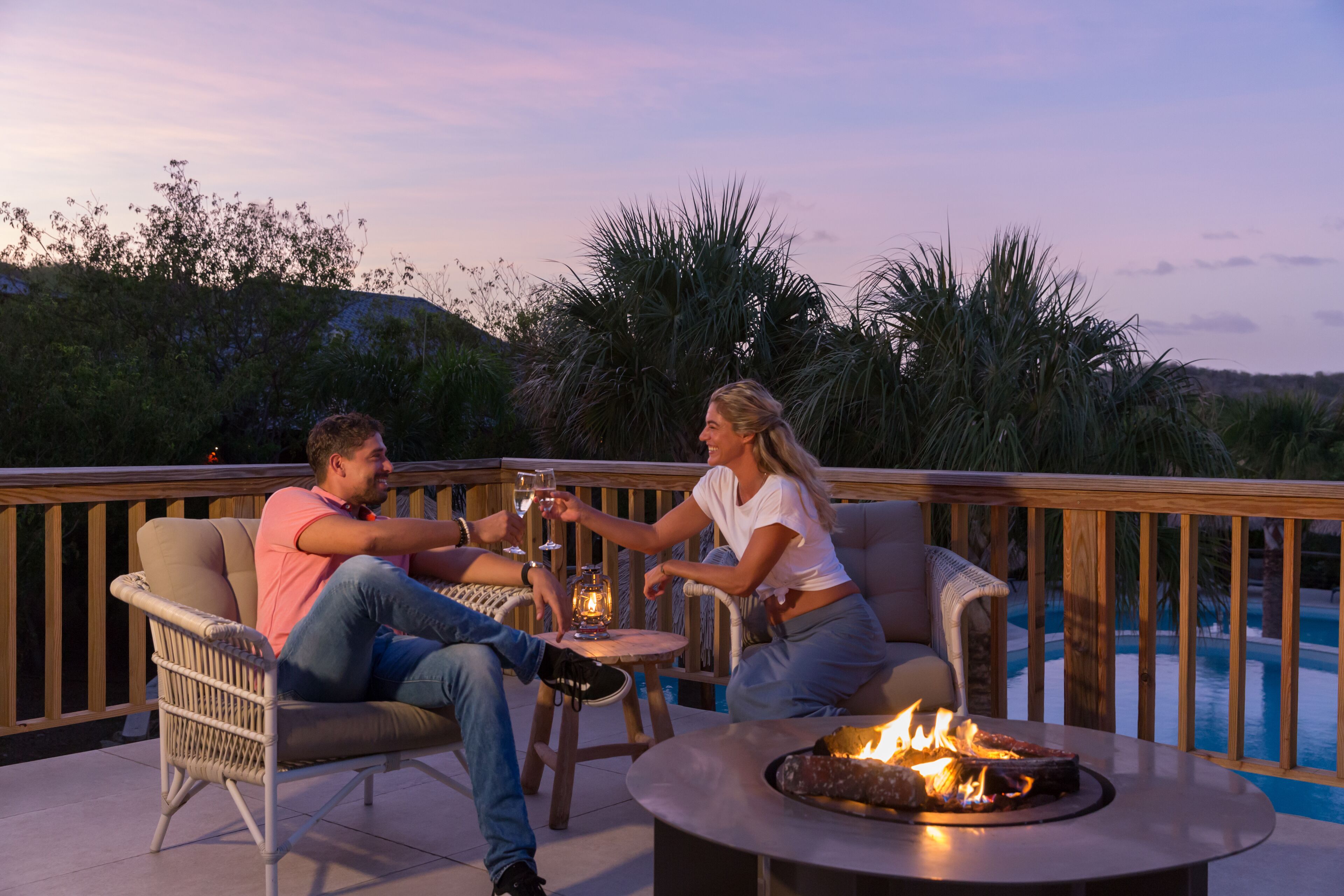 Um casal sentado à mesa, com uma fogueira, apreciando a vista da piscina.