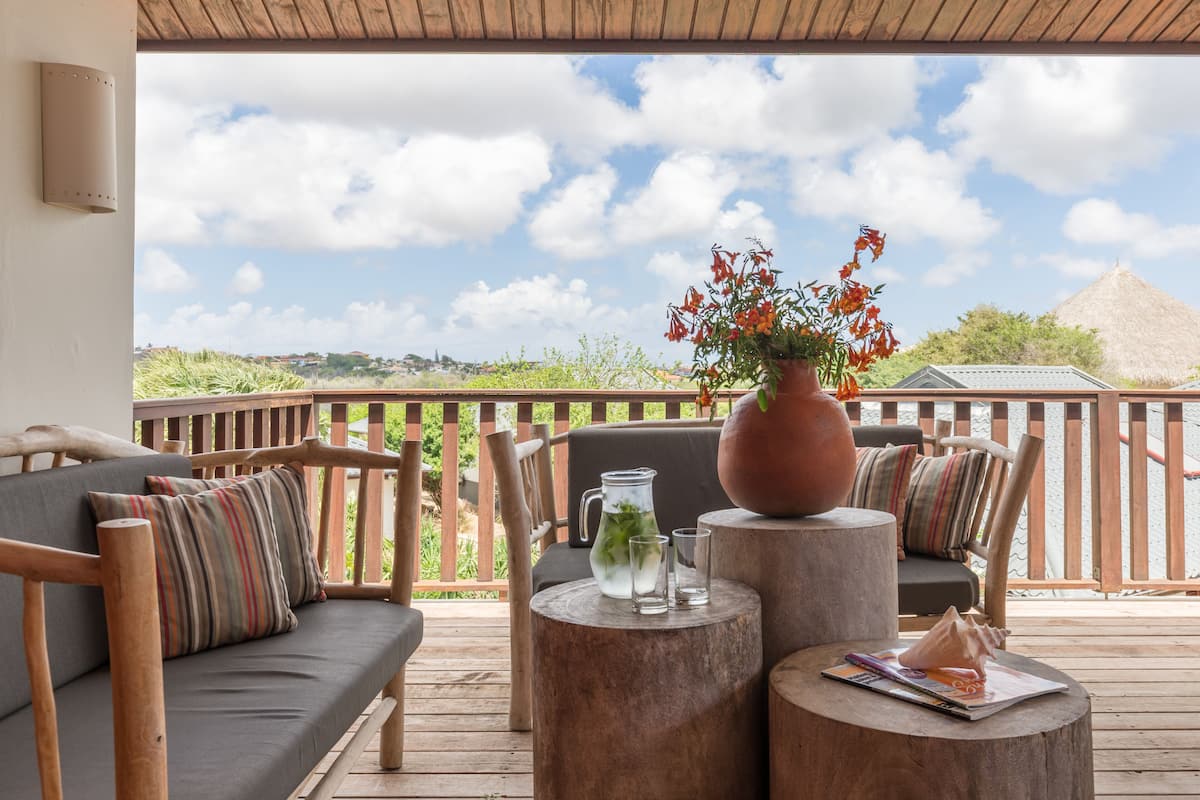 A wooden deck with a sofa and chairs, a table with a vase of flowers, and a view of the landscape.