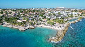 An aerial view of a coastal town with a beach, clear blue waters, and a mix of residential and commercial buildings. - Morena Resort (Jan Thiel)