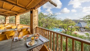 An outdoor dining area with wooden tables and chairs, a pool in the background, and a view of the surrounding greenery. - Morena Resort (Jan Thiel)