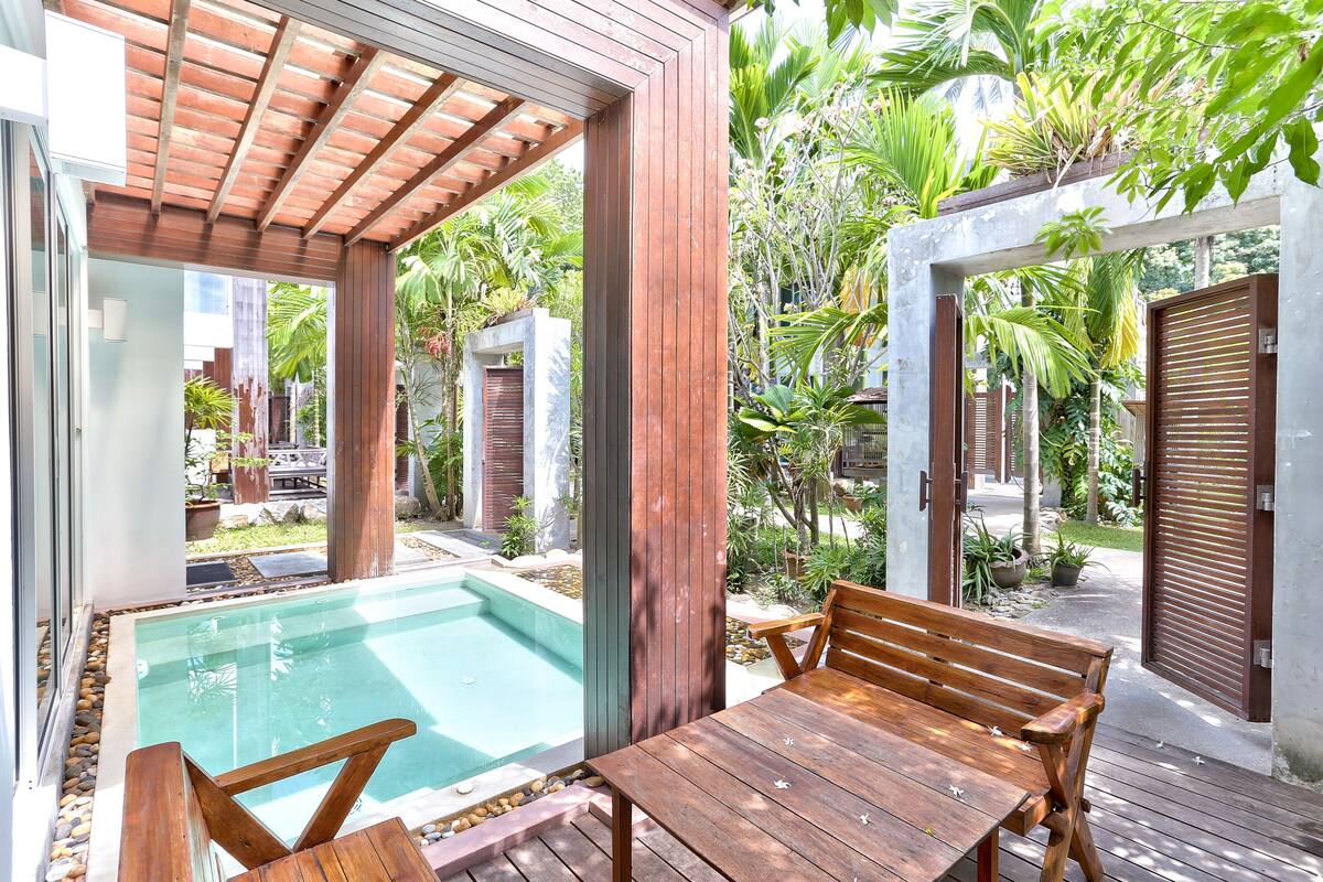 Eine Holzterrasse mit Pool, umgeben von üppiger Vegetation und einem Pergola.