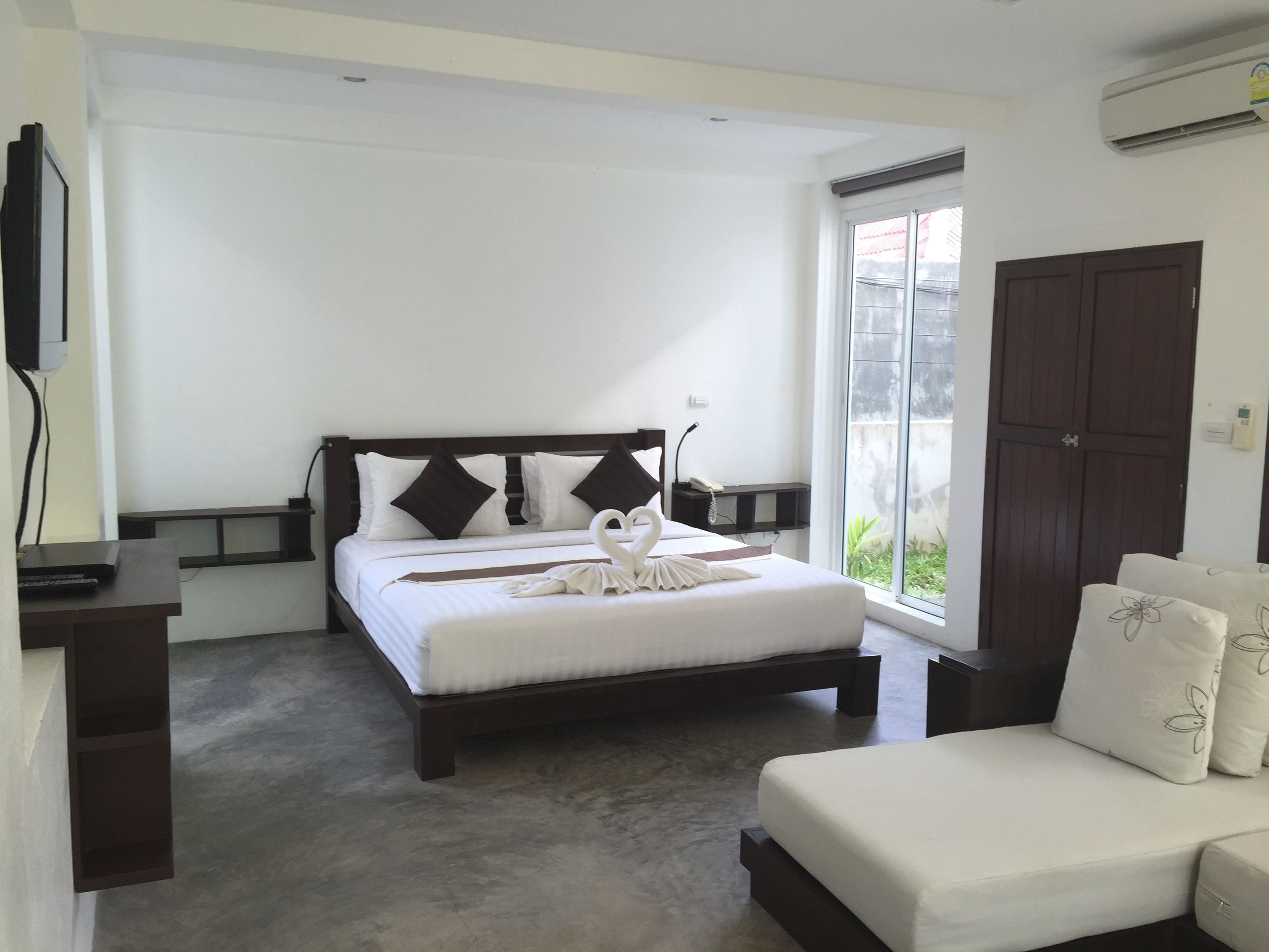 A bedroom with a bed, a bedside table, a chair, a wardrobe, and a large window.