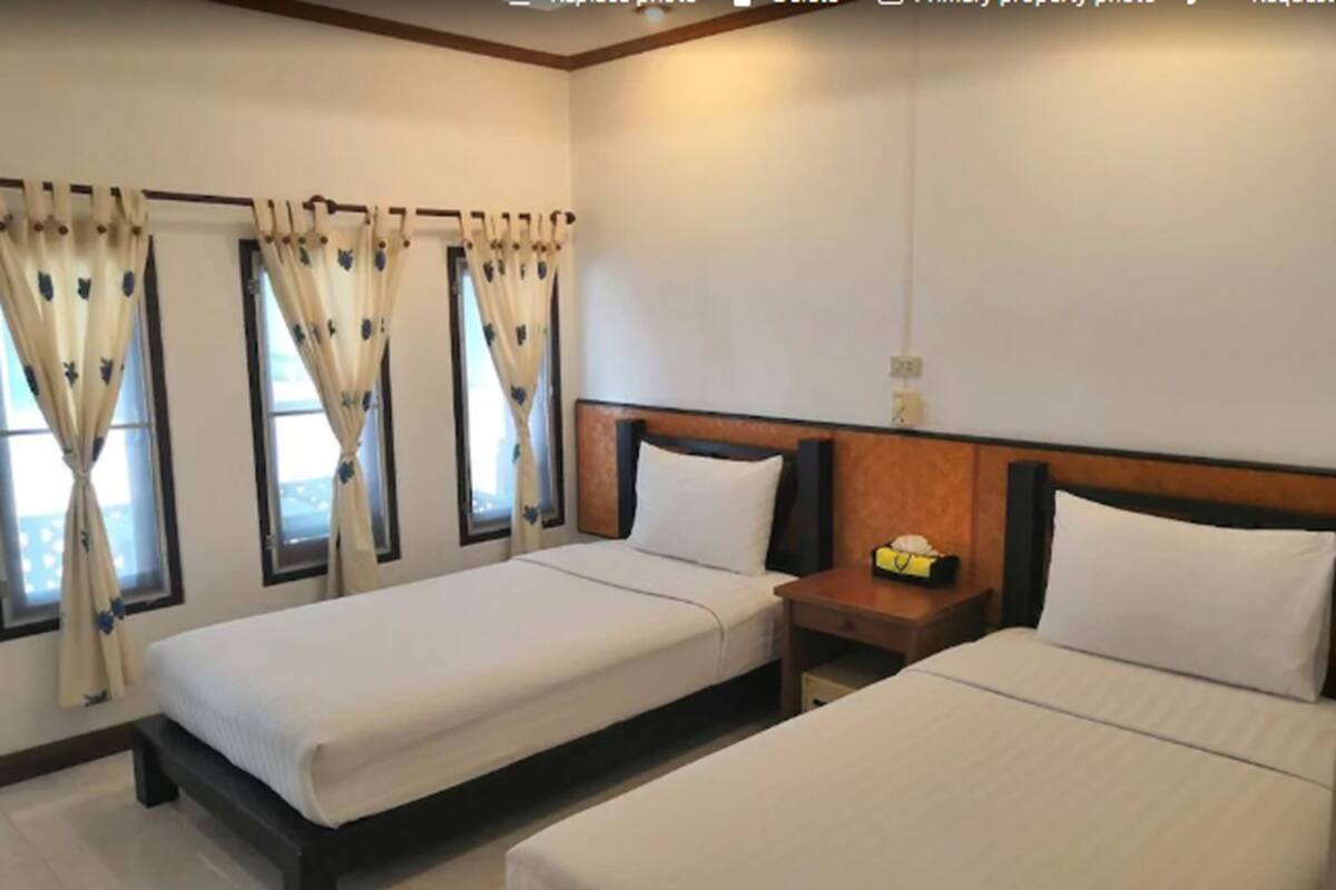 Ein Hotelzimmer mit zwei Betten, einem Holz-Kopfteil, einem Nachttisch mit Lampe und Vorhängen an den Fenstern.