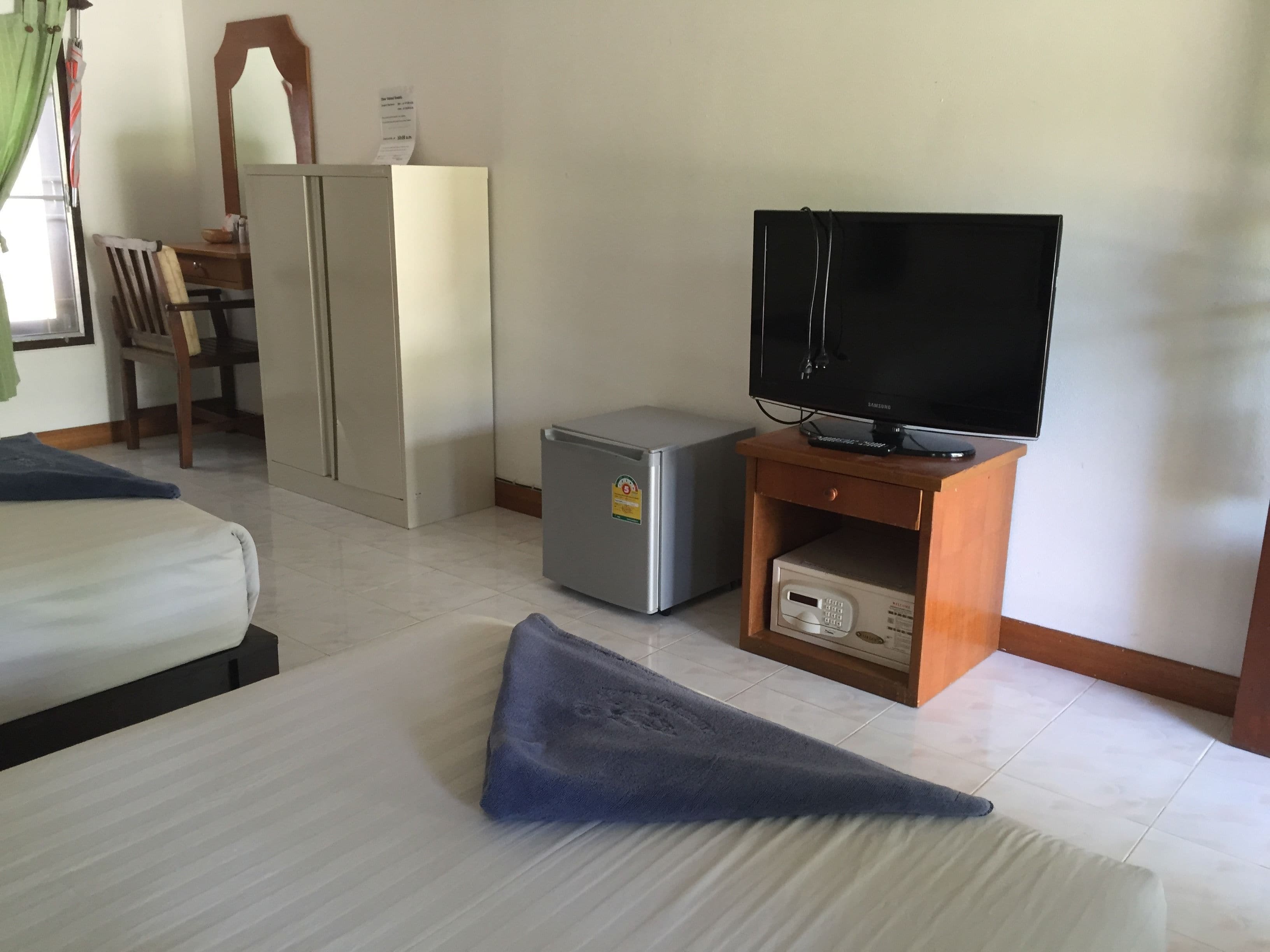 A hotel room with a bed, a TV on a wooden stand, a small fridge, and a desk with a chair.