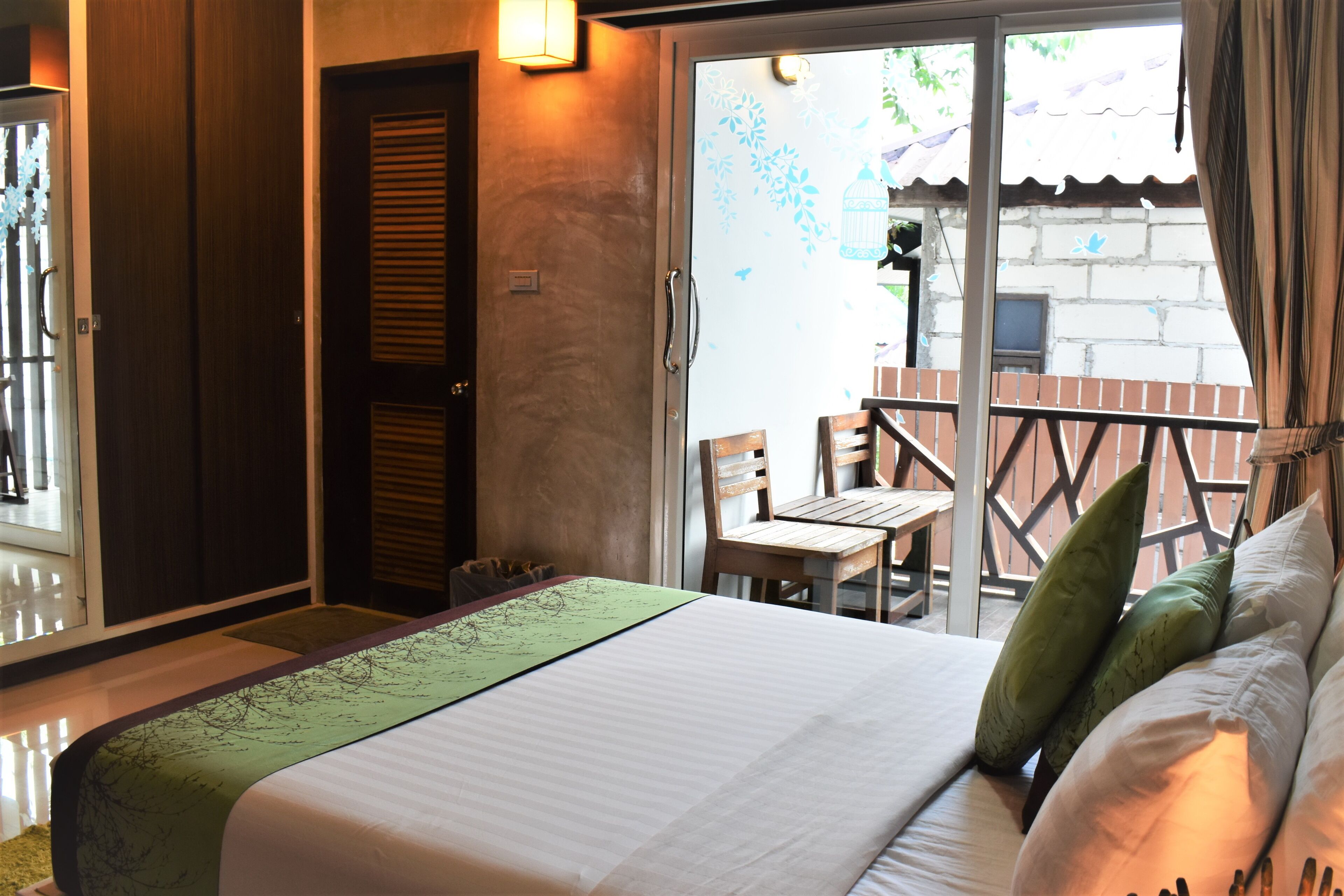 Habitación de hotel con cama, una silla de madera, balcón con vistas al exterior y una puerta con ventanal de vidrio esmerilado.