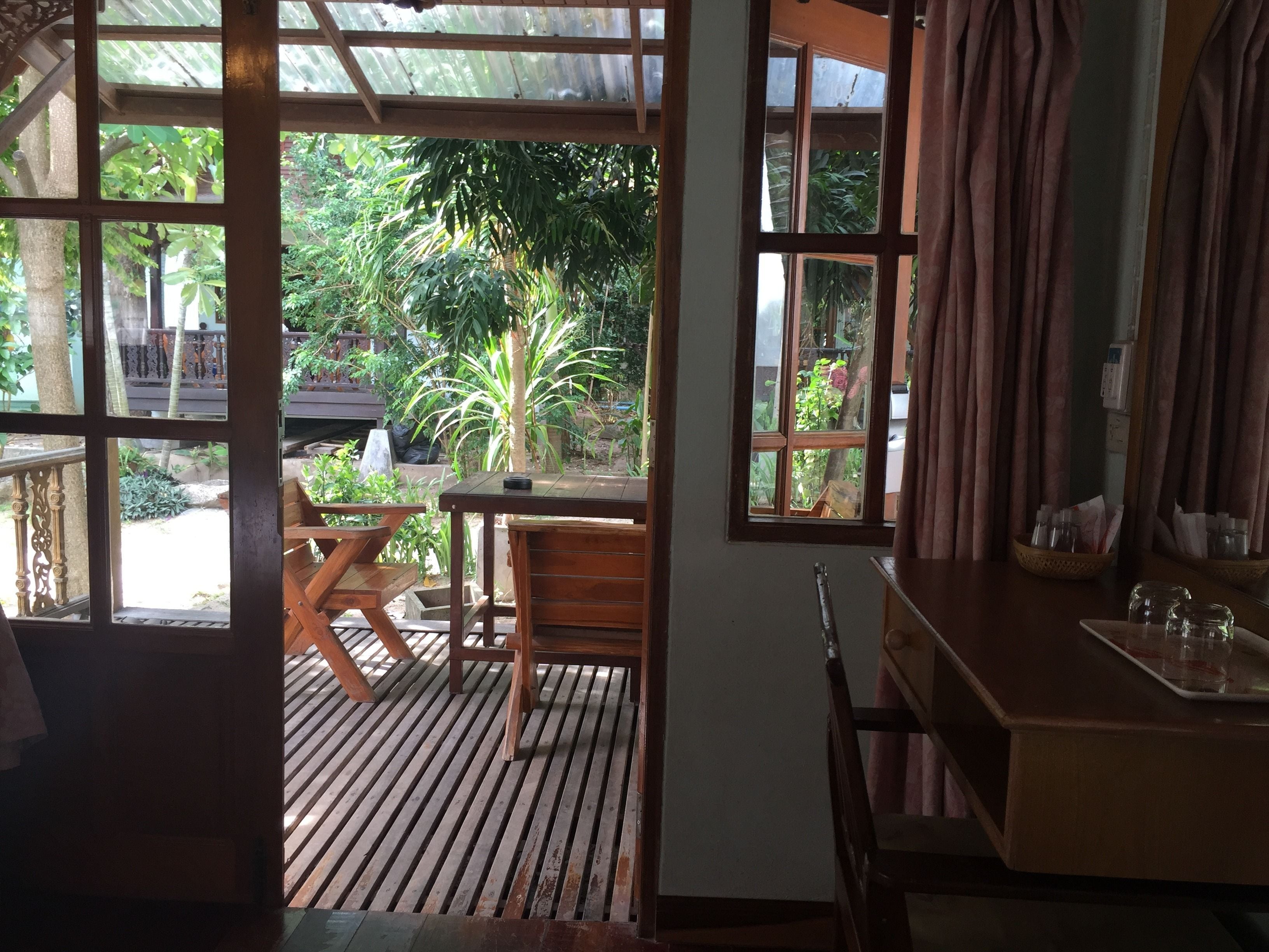 A wooden deck with a table and chairs, a small table with a tray, and a view of a garden through a window.