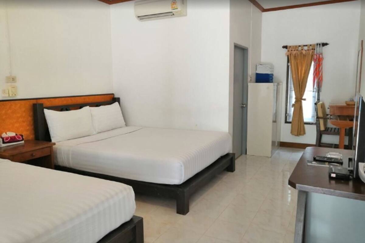 Ein Hotelzimmer mit zwei Betten, einem Schreibtisch mit Stuhl, einem kleinen Kühlschrank und einer Klimaanlage an der Wand.
