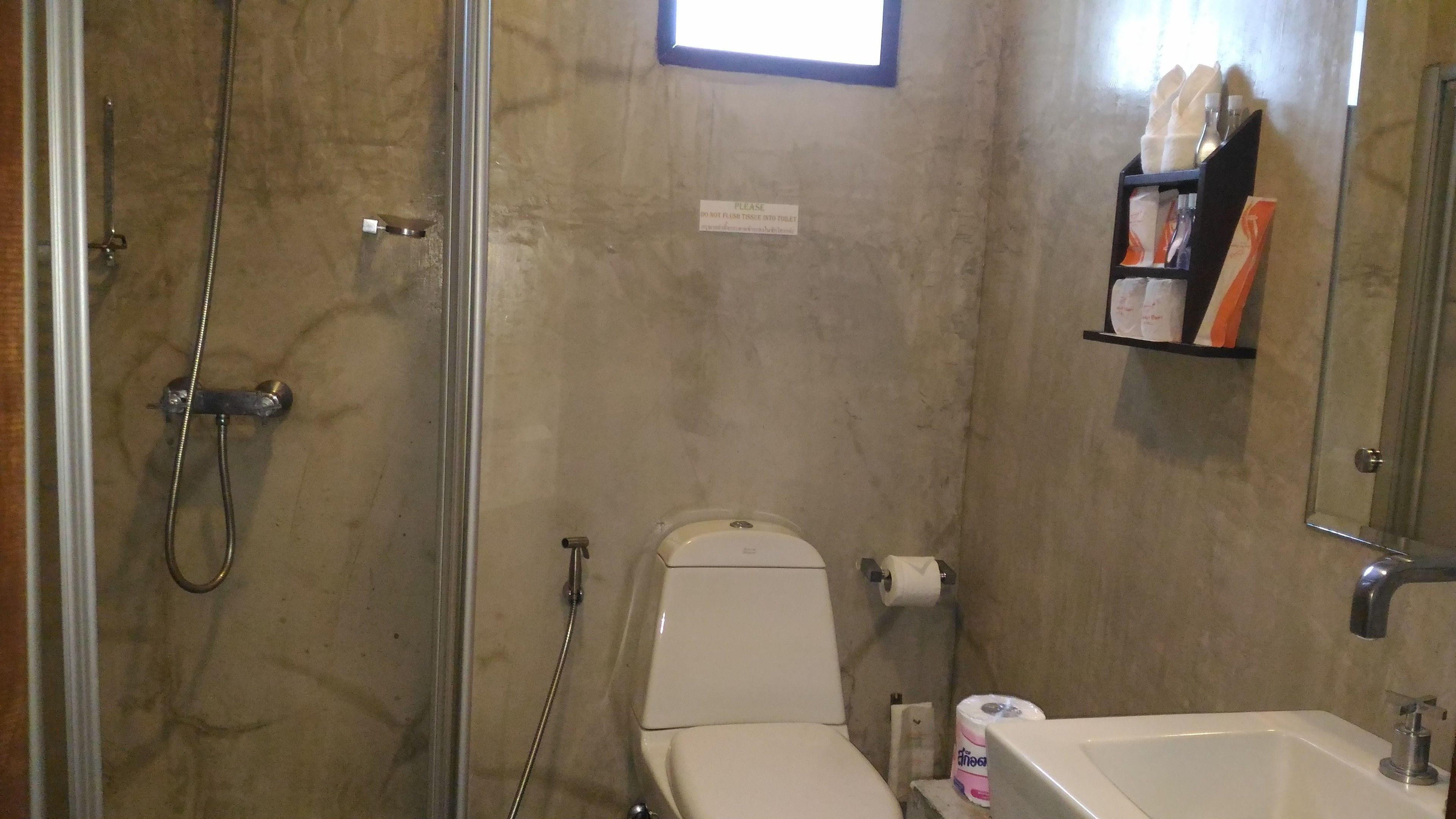Een badkamer met douche, toilet en wastafel. Er hangt een bord aan de muur en een plank met toiletartikelen.