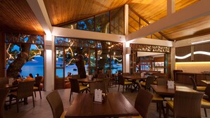 Un restaurant avec des tables et des chaises en bois, de grandes fenêtres donnant sur la mer et un décor intérieur moderne.