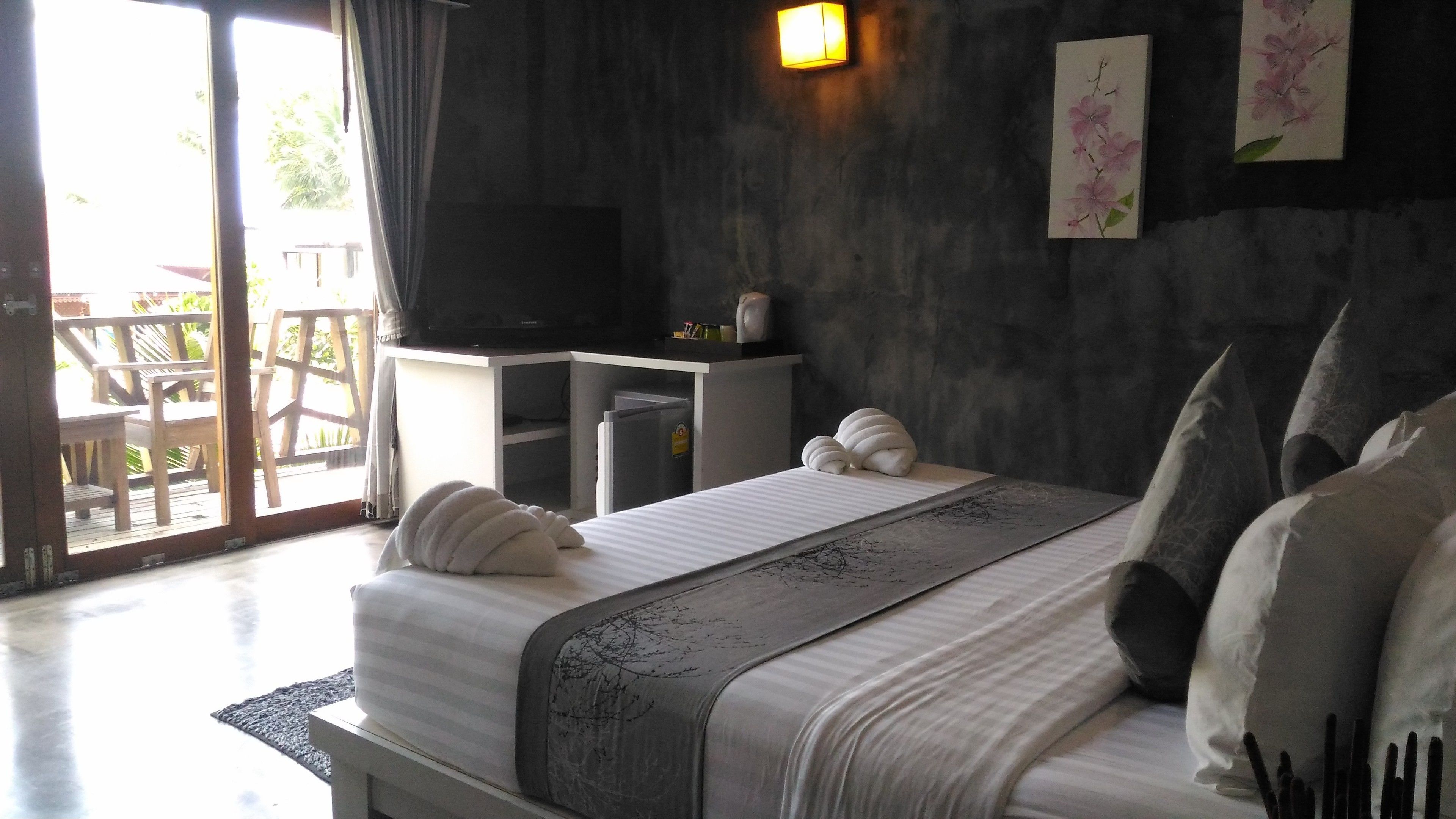 Un dormitorio con cama, televisor, escritorio y balcón.