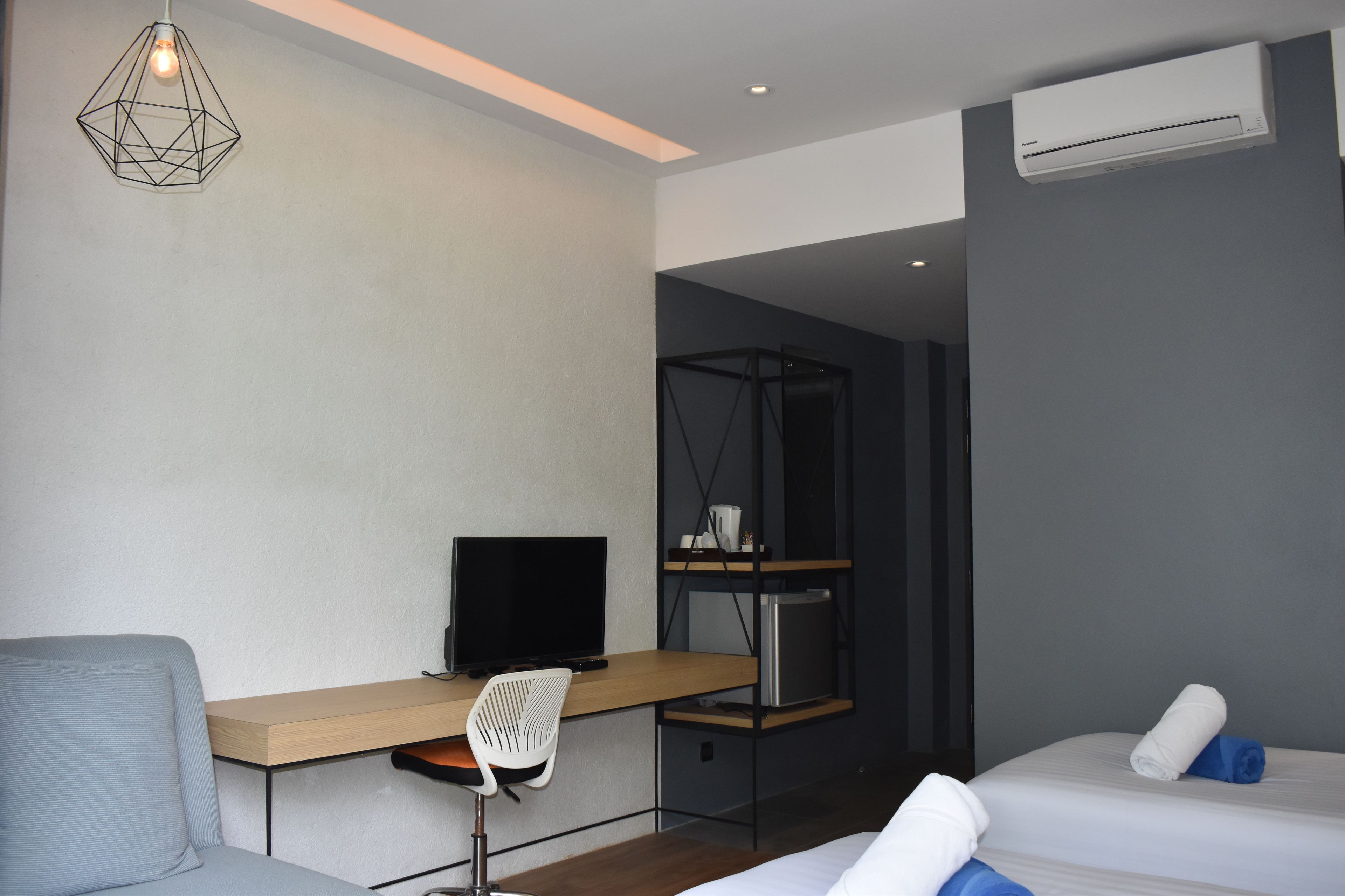 A modern hotel room with a desk, chair, bed, and an air conditioning unit.