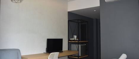 A modern hotel room with a desk, chair, bed, and an air conditioning unit.