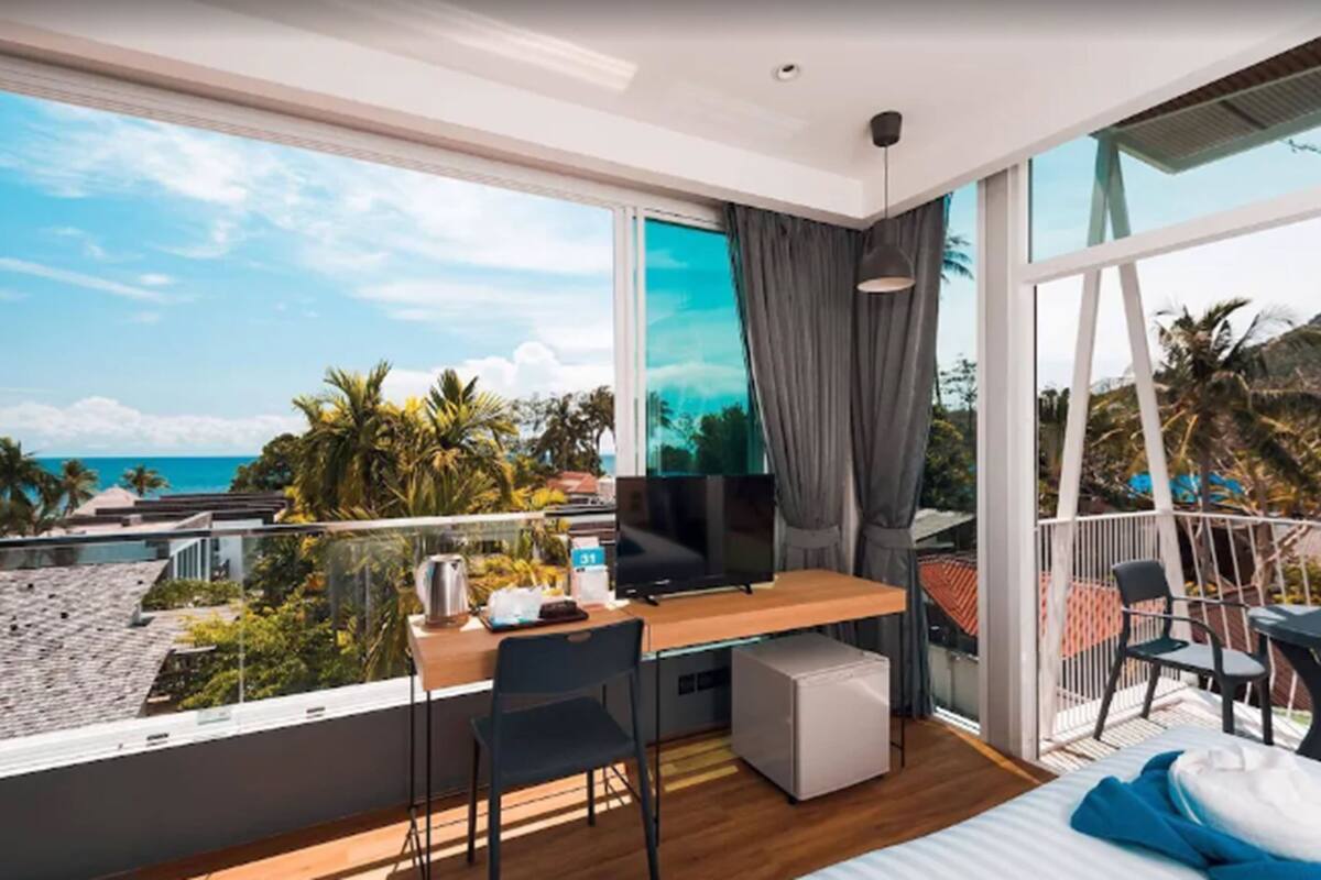 Ein modernes Hotelzimmer mit großem Balkon, Schreibtisch, Fernseher und Bett.