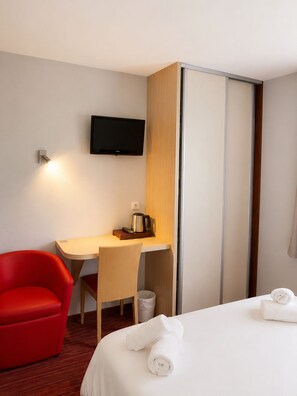 Une chambre d’hôtel avec un lit, un bureau avec une télévision, une chaise rouge et une armoire.