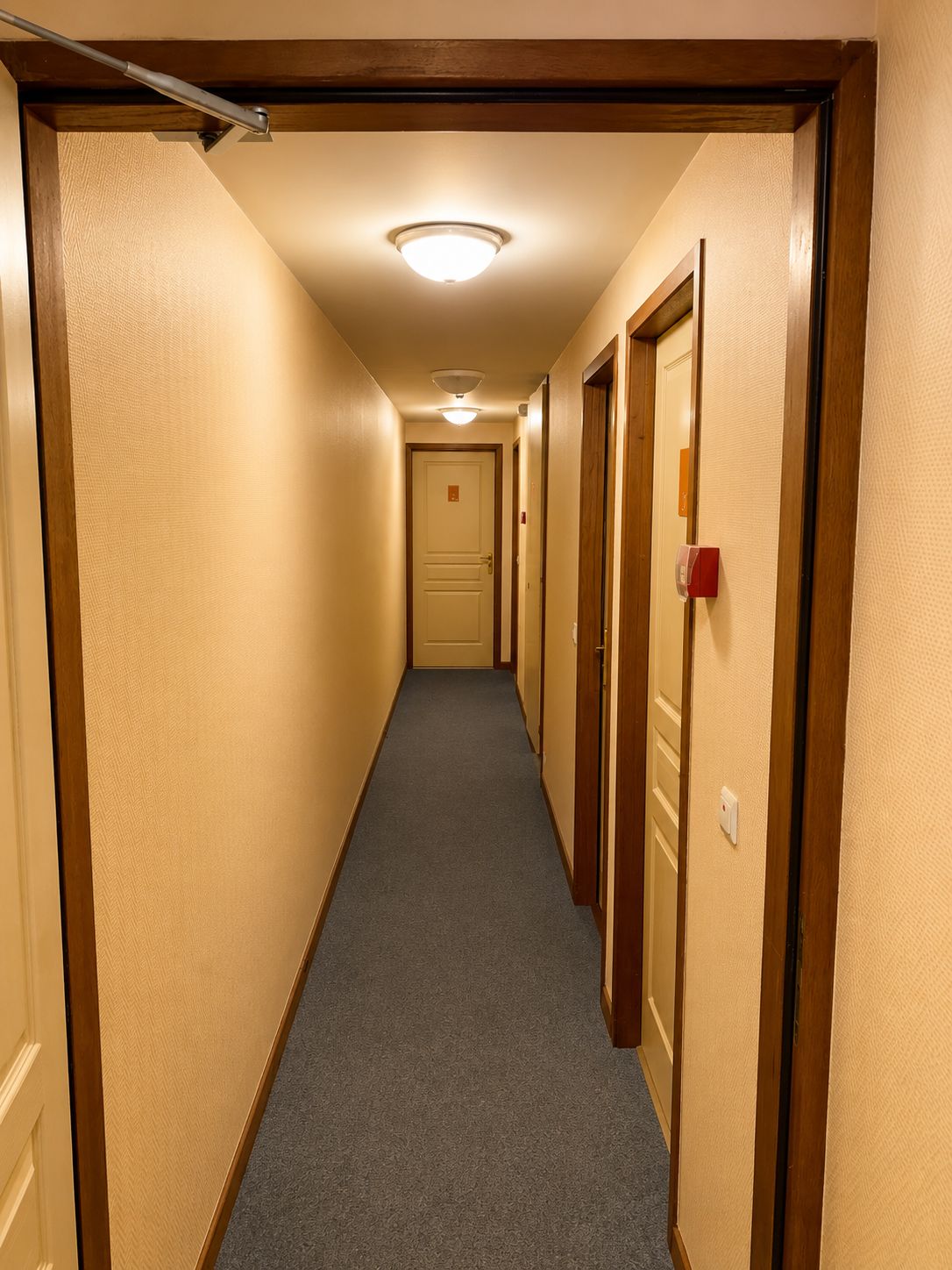 Ein Hotelgang mit Teppichböden, Holztüren und einer Deckenleuchte.