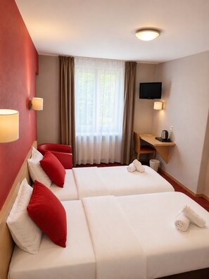 Une chambre d’hôtel avec deux lits, un bureau, une télévision et une fenêtre avec des rideaux.