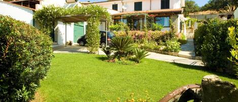 Ein Wohnhaus mit gepflegtem Rasen, einer überdachten Terrasse und verschiedenen Pflanzen und Blumen.