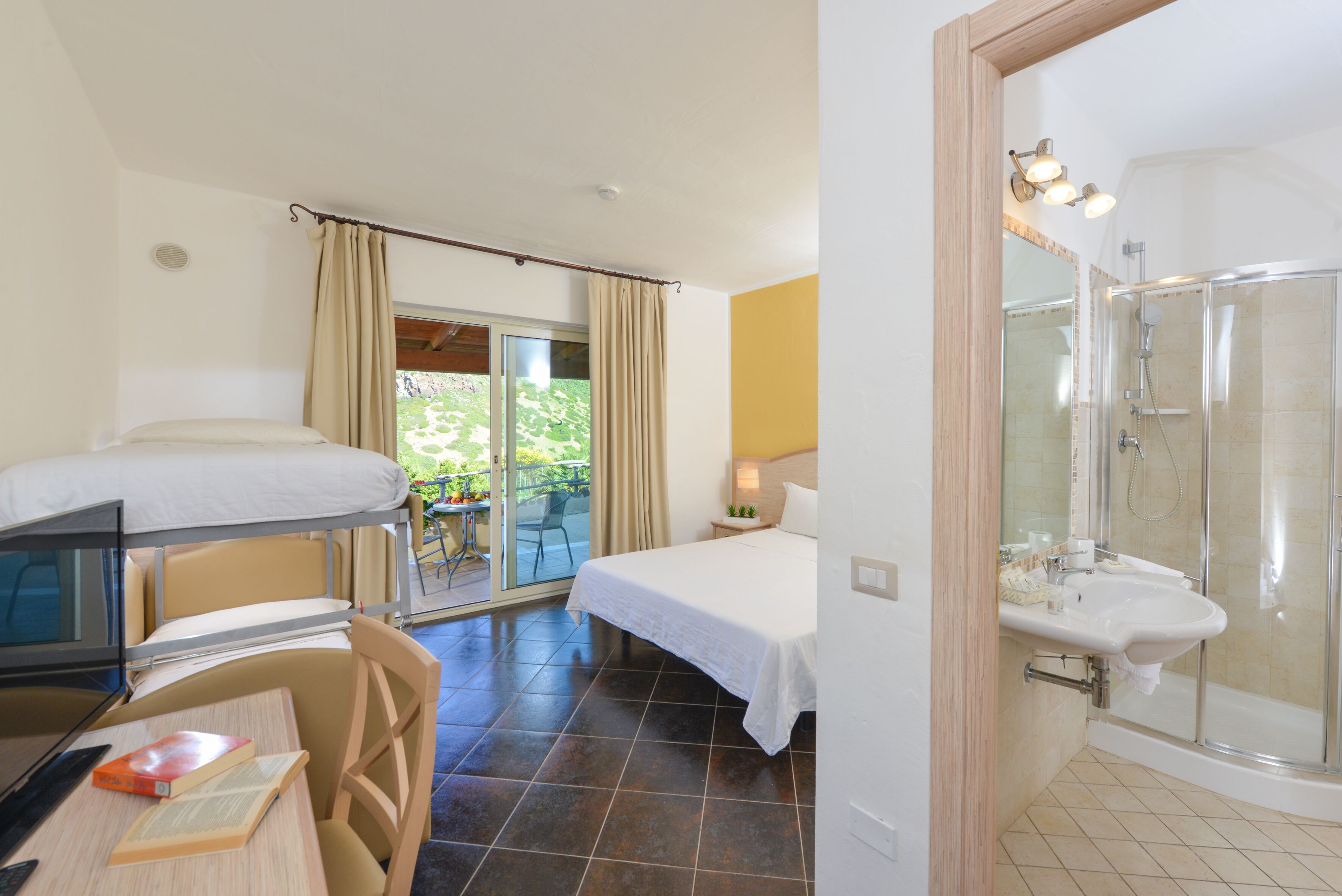 Une chambre d’hôtel comprenant un lit, un bureau avec un ordinateur portable et des livres, un espace douche et un balcon avec des rideaux.