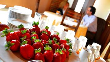 Una mesa de comedor con un plato de fresas y tazas blancas.
