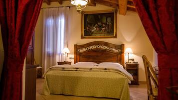 A bedroom with a wooden headboard, two bedside lamps, a bed with a green bedspread, a painting above the bed, and red curtains framing the window.