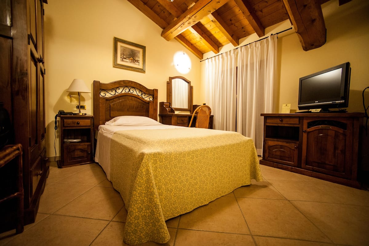 A hotel room with a bed, a television, a desk with a lamp, a chair, and wooden cabinets.