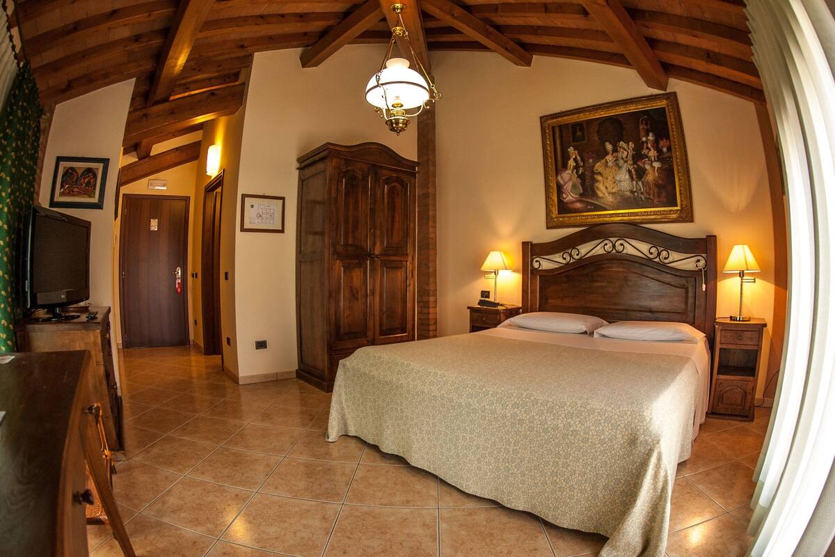 A bedroom with a large bed, wooden headboard, two bedside tables with lamps, a wooden wardrobe, and a painting on the wall.